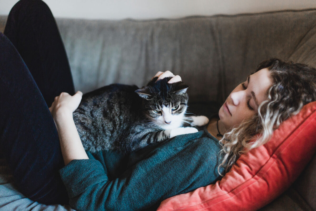 A woman lying on the couch while petting her cat that's lying on her chest