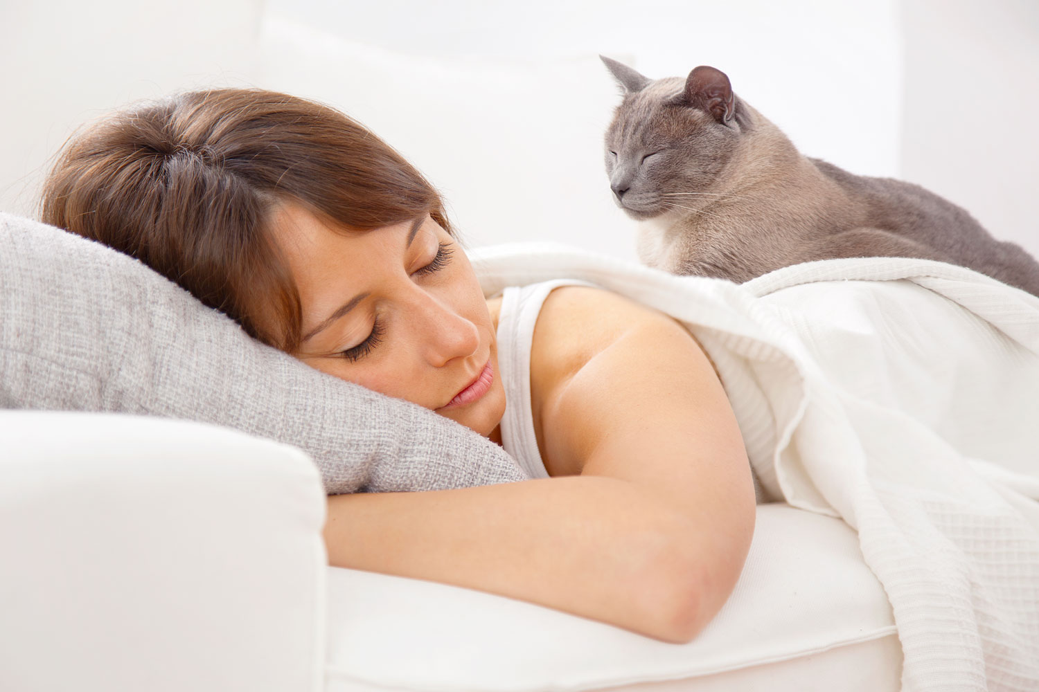 Woman sleeping on her bed with her cat lying on her back