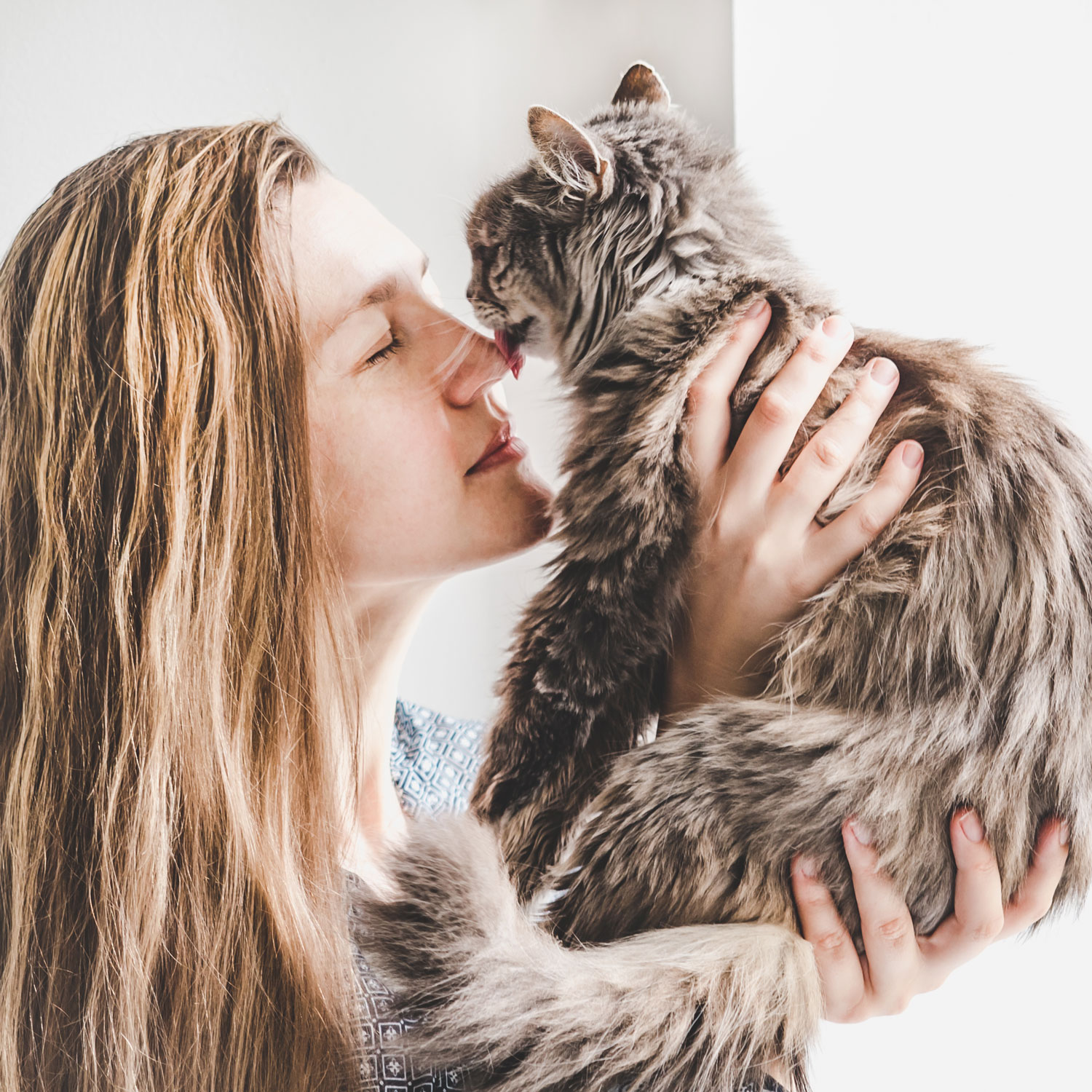 A woman holding her cat close to her nose and licking her